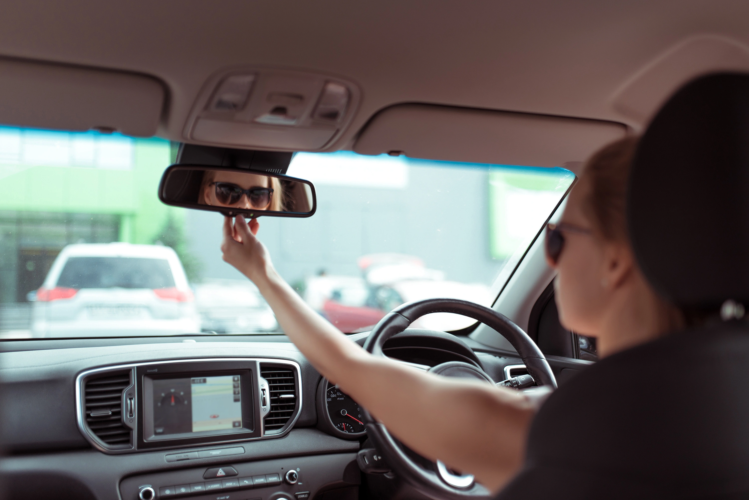 girl in passenger compartment of car looks into bright light of rear view, checks children in back row of seats, parking shopping center, reversing car. Woman in summer sunglasses in cit